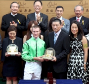 Executive Director of the Oriental Watch Holdings Limited Mr Alain Lam Hing Lun, accompanied by his wife, presents a souvenir to jockey Zac Purton.