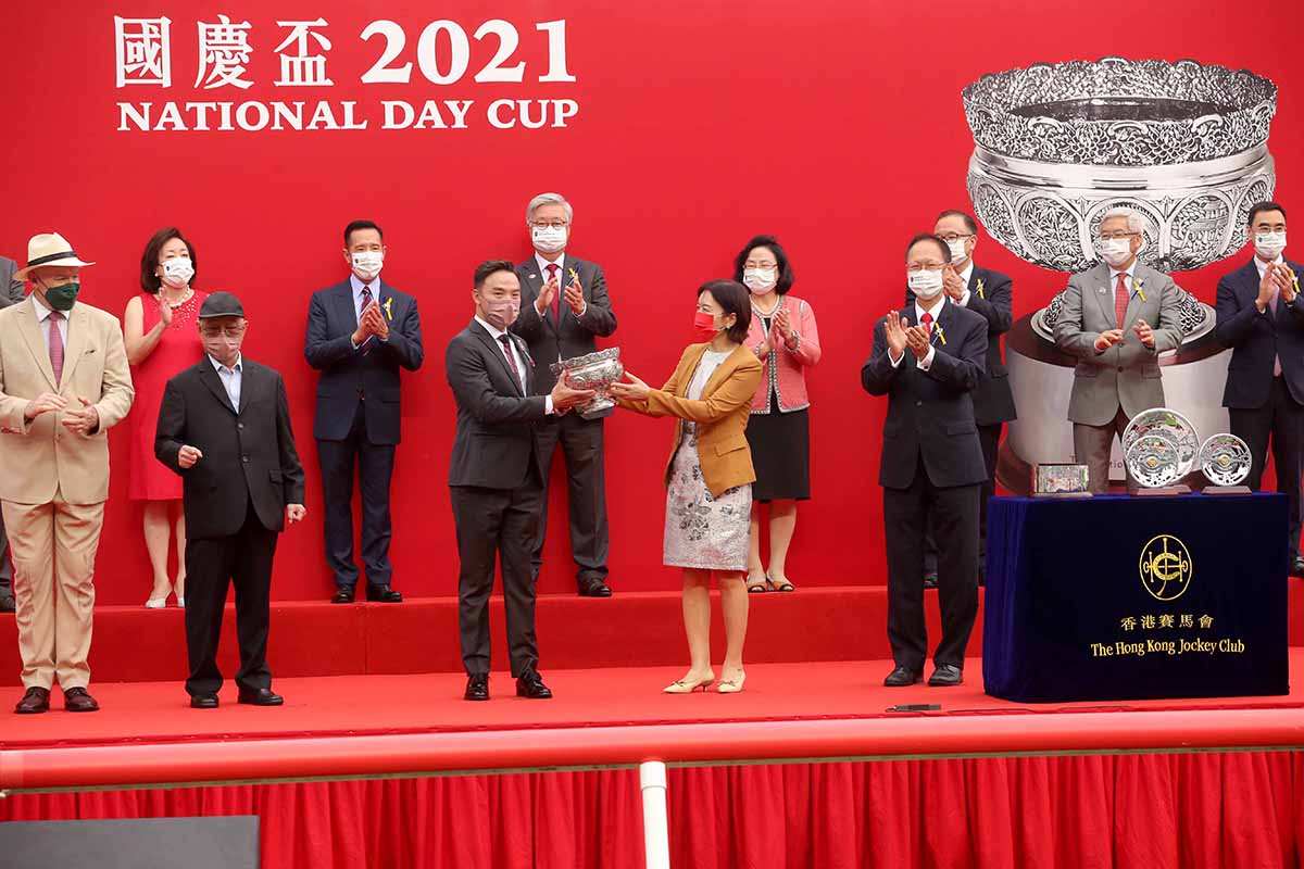中央人民政府駐香港特別行政區聯絡辦公室副主任盧新寧女士，將國慶盃的獎盃頒發予勝出馬匹「聚才」的馬主梁冠華。